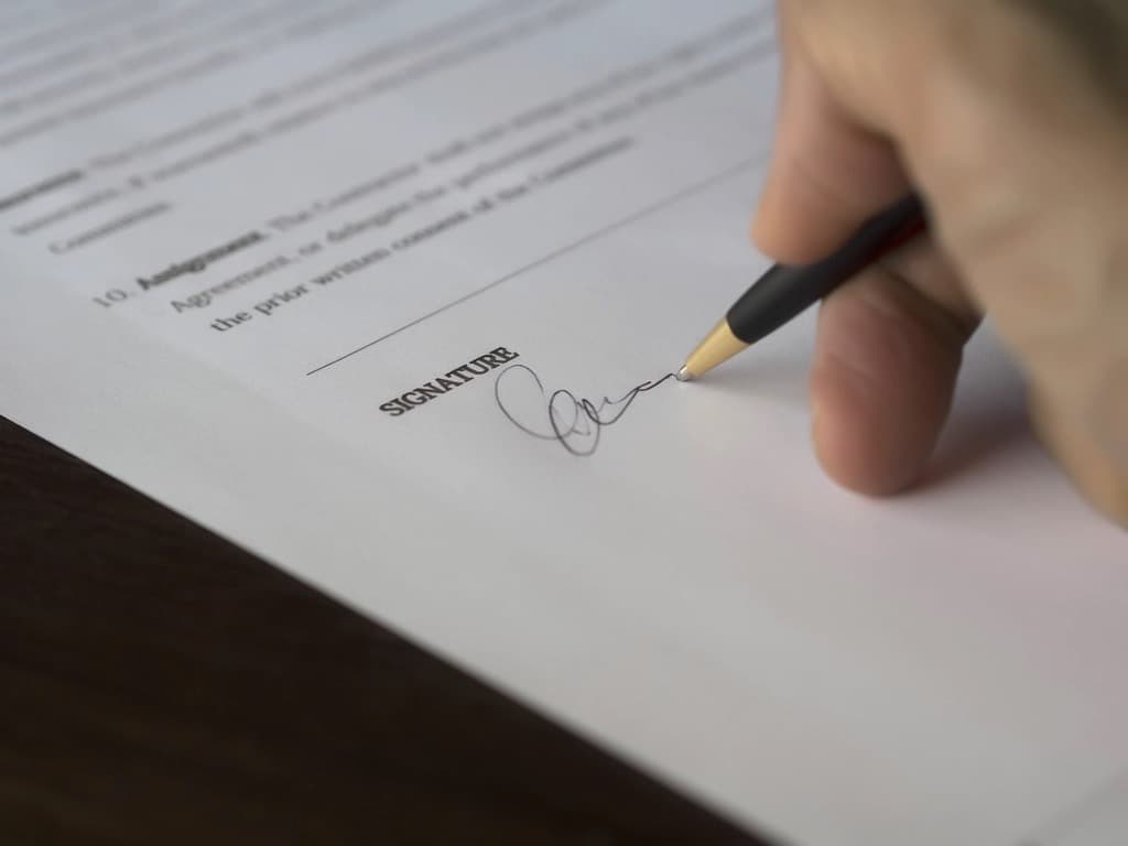 Close-up of a hand signing the signature line of a printed legal agreement with a pen, representing e-signed engagement letters and tax returns