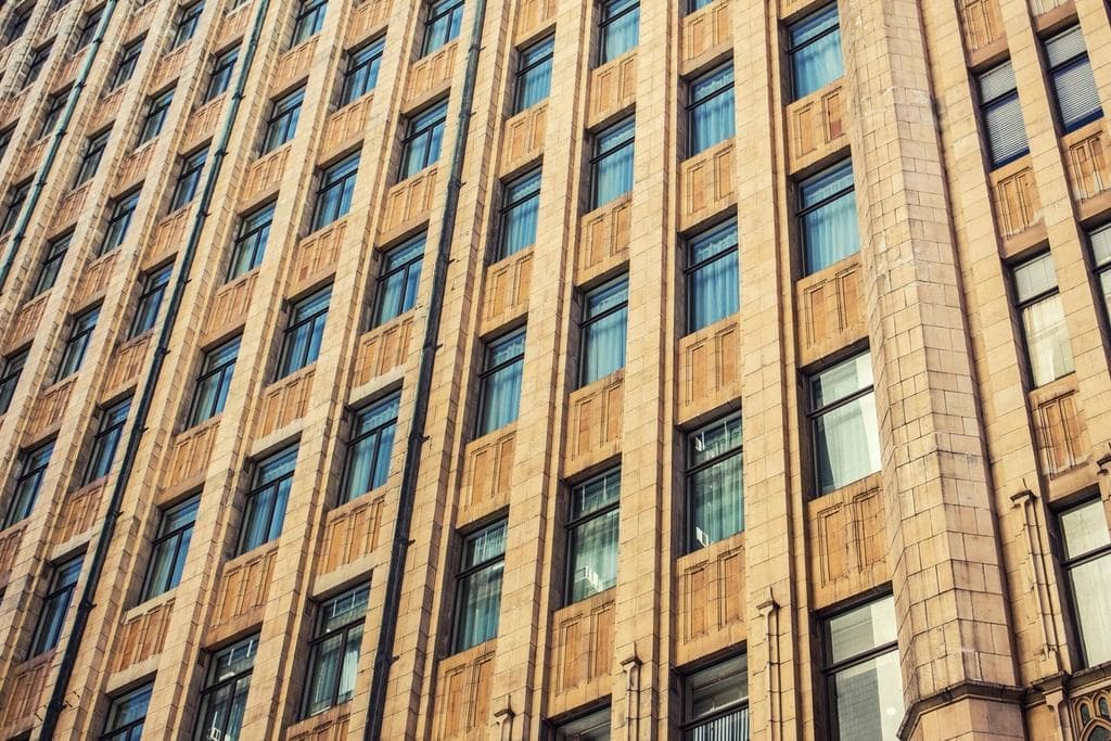 Low-angle view of a tan brick multi-story building facade with rows of windows, representing commercial real estate property