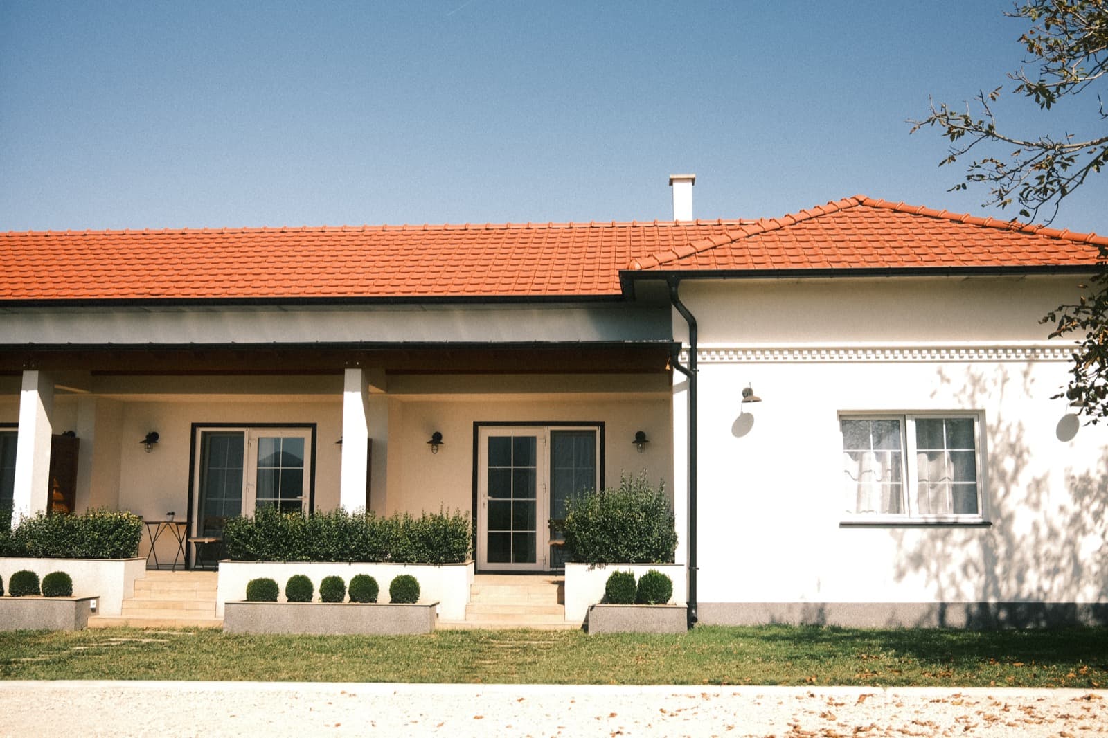 Modern single-story home with white walls, a red tile roof, covered porch and landscaped garden under a clear blue sky, a featured residential listing