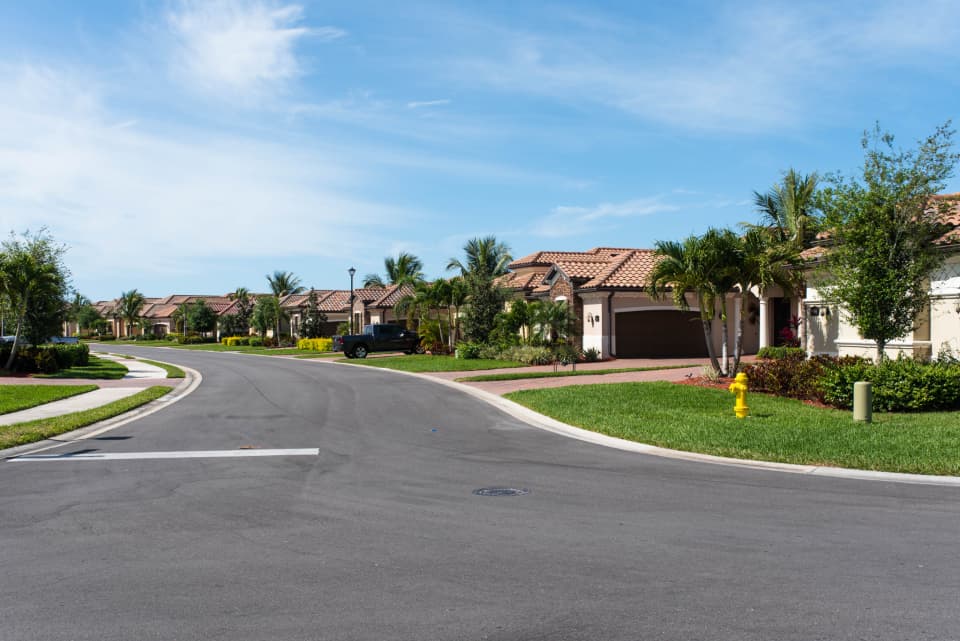 Sunny suburban neighborhood street lined with tile-roofed homes and palm trees, representing a residential real estate market or property portal