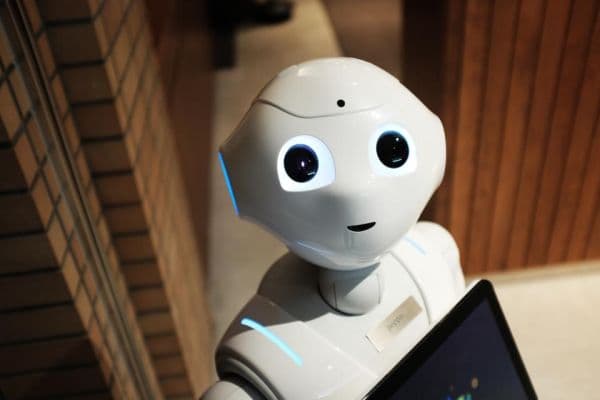 Friendly white humanoid robot with large round eyes and a tablet on its chest, representing an AI assistant