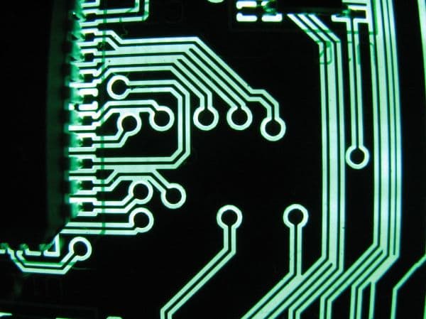 Macro shot of glowing green circuit-board traces and connection pads on a black background
