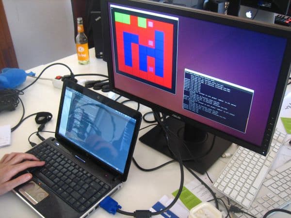 Two-screen developer desk with a laptop and a monitor showing a colourful grid and a scrolling terminal window