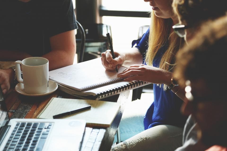 Small team around a cafe table with a laptop and notebooks, as a sales team working incoming leads together