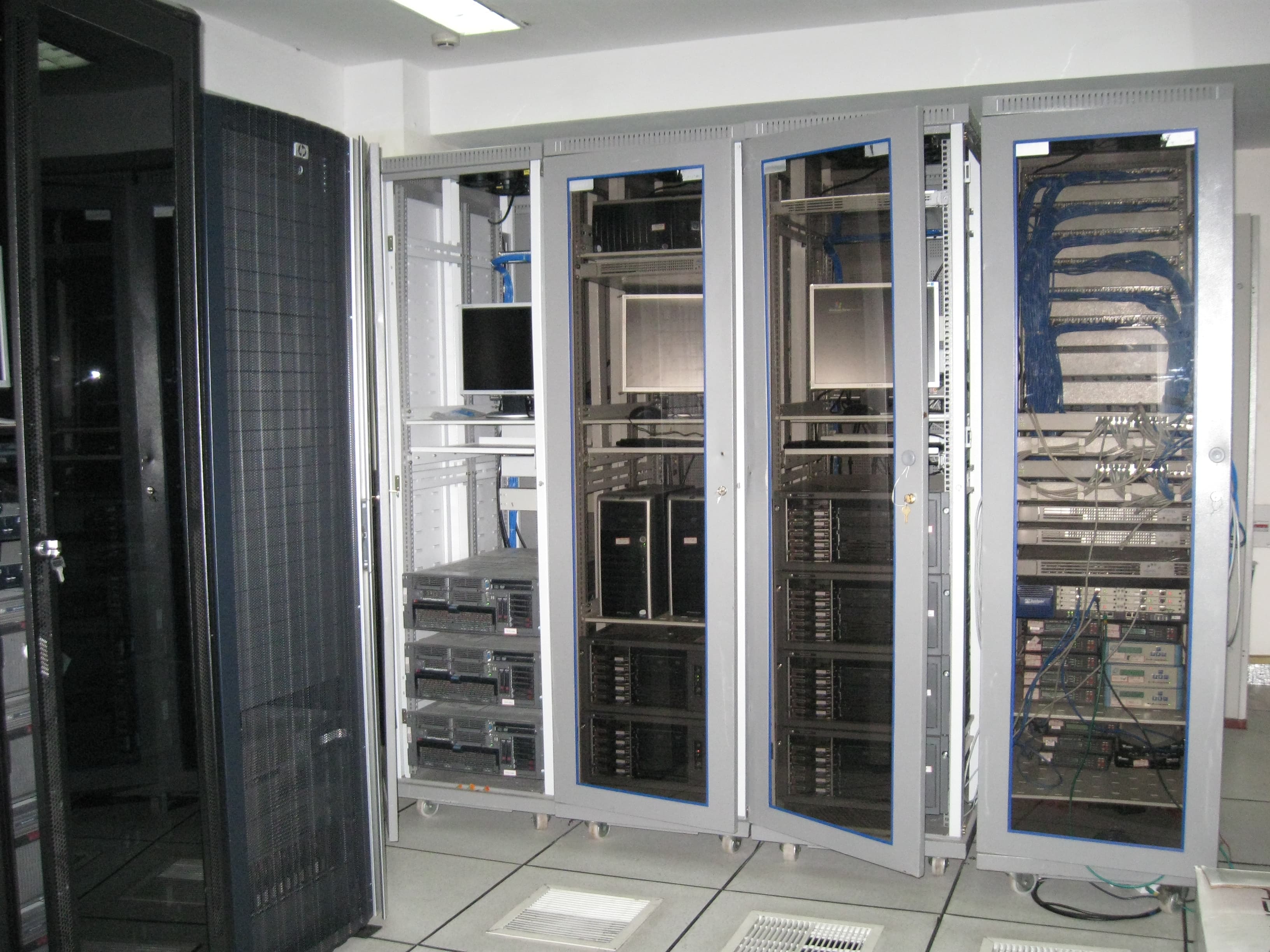 Row of open server racks in a data room with cabling, disk arrays and a monitor, self-hosted hardware