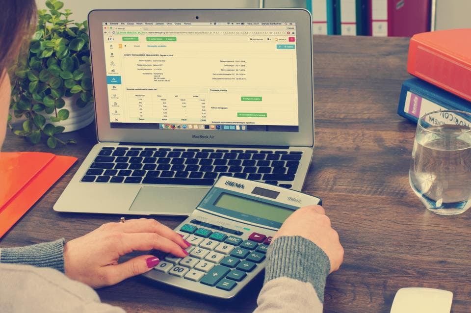 Person using a desk calculator beside a laptop showing accounting and invoice software, as orders post into the books
