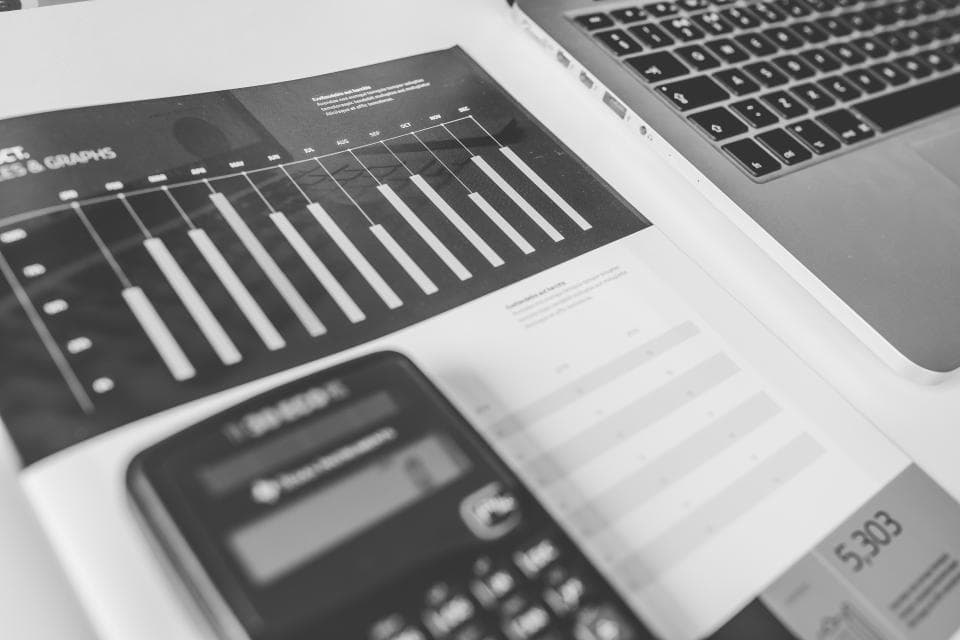 Black and white financial report with bar charts beside a calculator and laptop, for reconciliation and month-end books