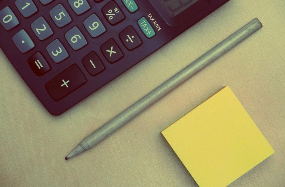 Close-up of a calculator with a tax-rate button, a pencil and a sticky note, for GST calculation and bookkeeping