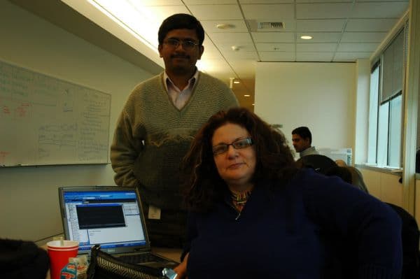Two office colleagues beside a laptop running business software in front of a whiteboard of diagrams