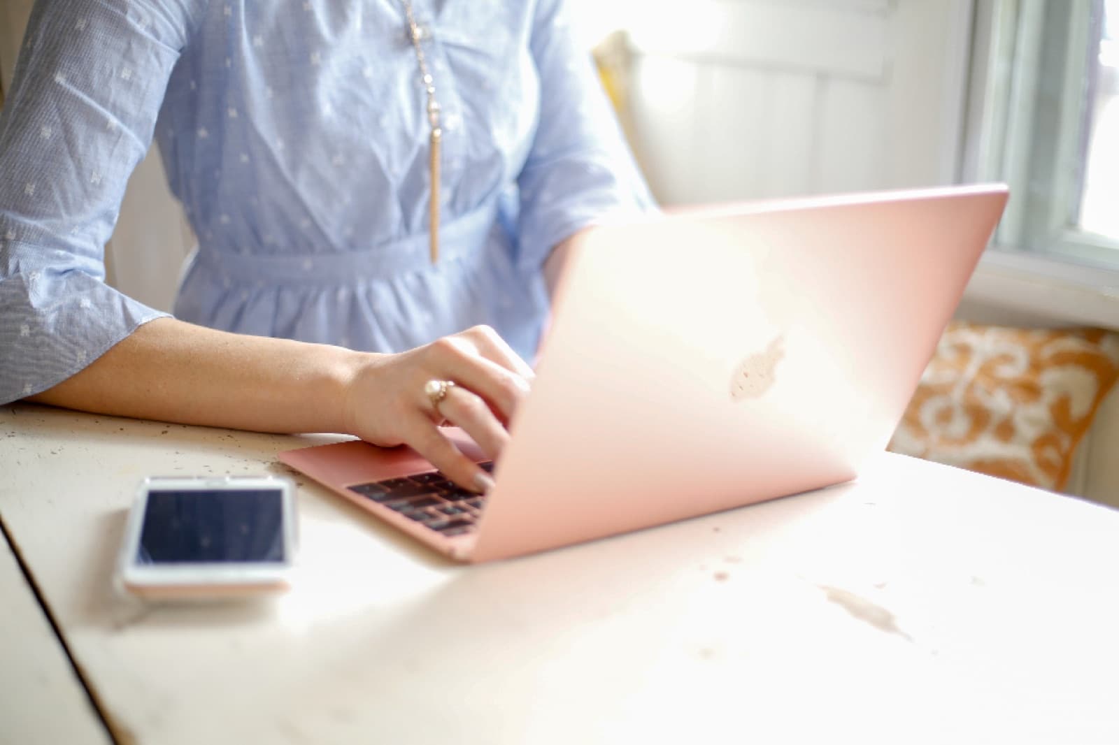 Person typing on a laptop at a sunlit desk with a smartphone beside them, as real-time notifications reach the team