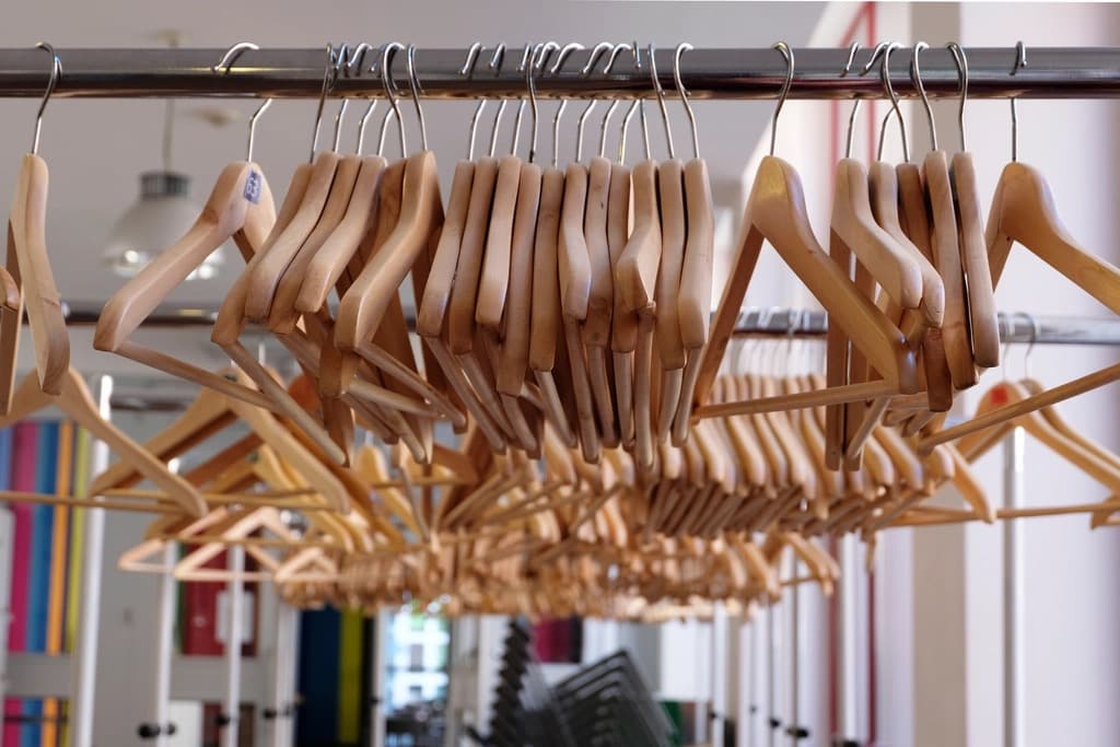 Close-up of dozens of empty wooden garment hangers packed along a metal clothing rail in a bright fashion store