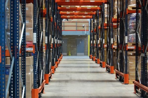 Interior aisle of a distribution warehouse lined with tall industrial shelving racks holding cartons