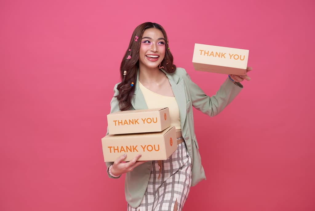 Smiling online seller holding a stack of kraft shipping boxes marked Thank You