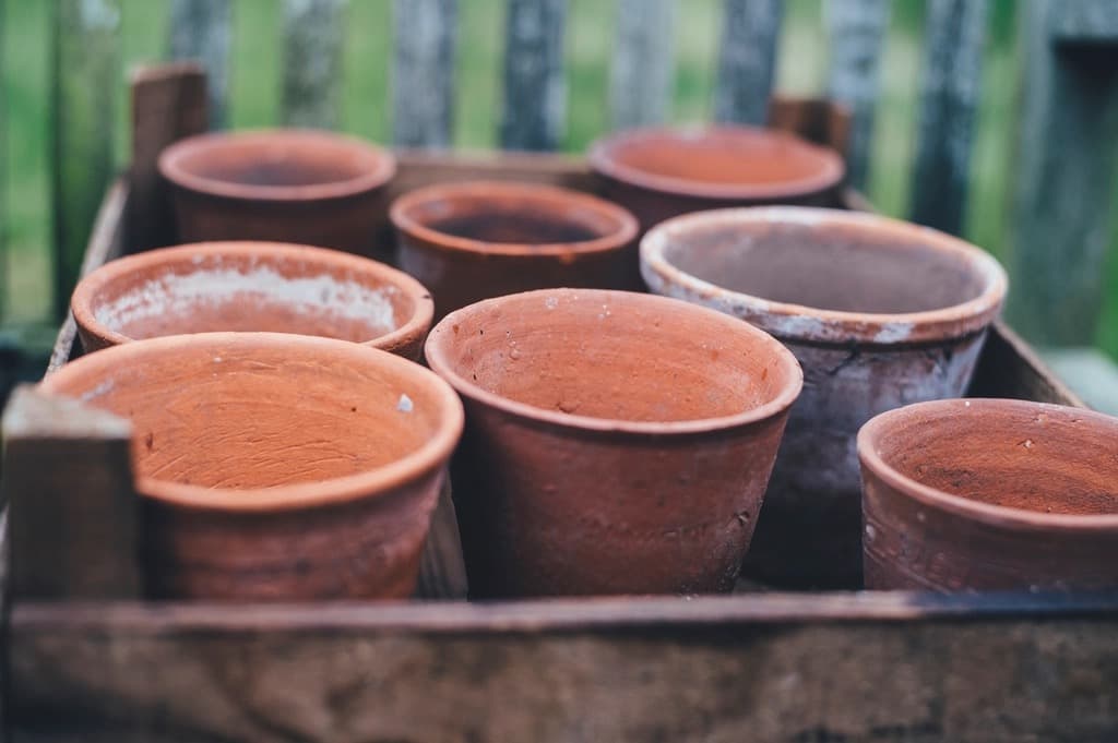 A wooden crate holding rows of handmade terracotta clay pots outdoors