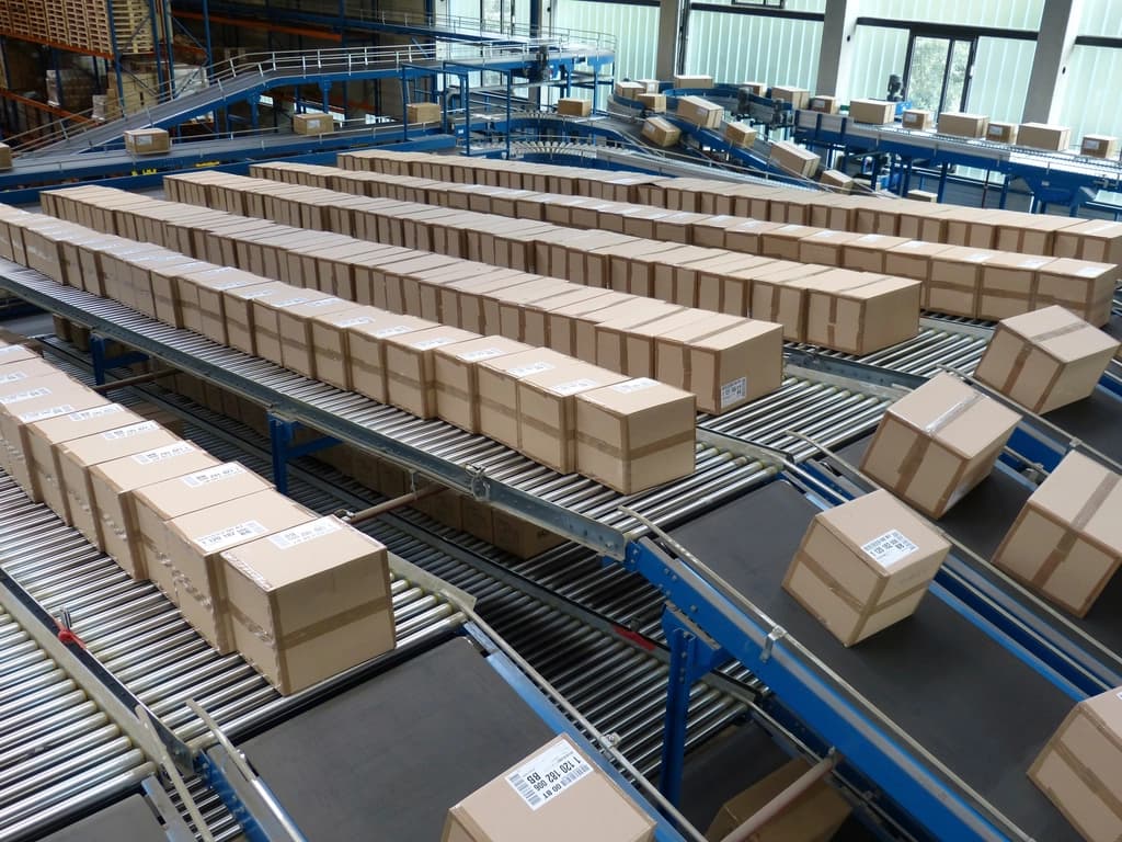 Rows of identical sealed cardboard cartons travelling along a roller conveyor sortation line in a distribution centre