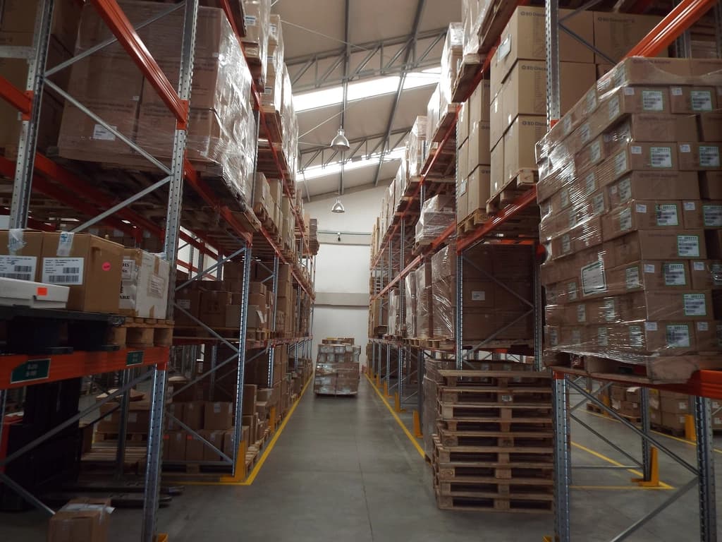 Long aisle of tall pallet racking filled with shrink-wrapped cartons and boxed goods inside a B2B wholesale warehouse