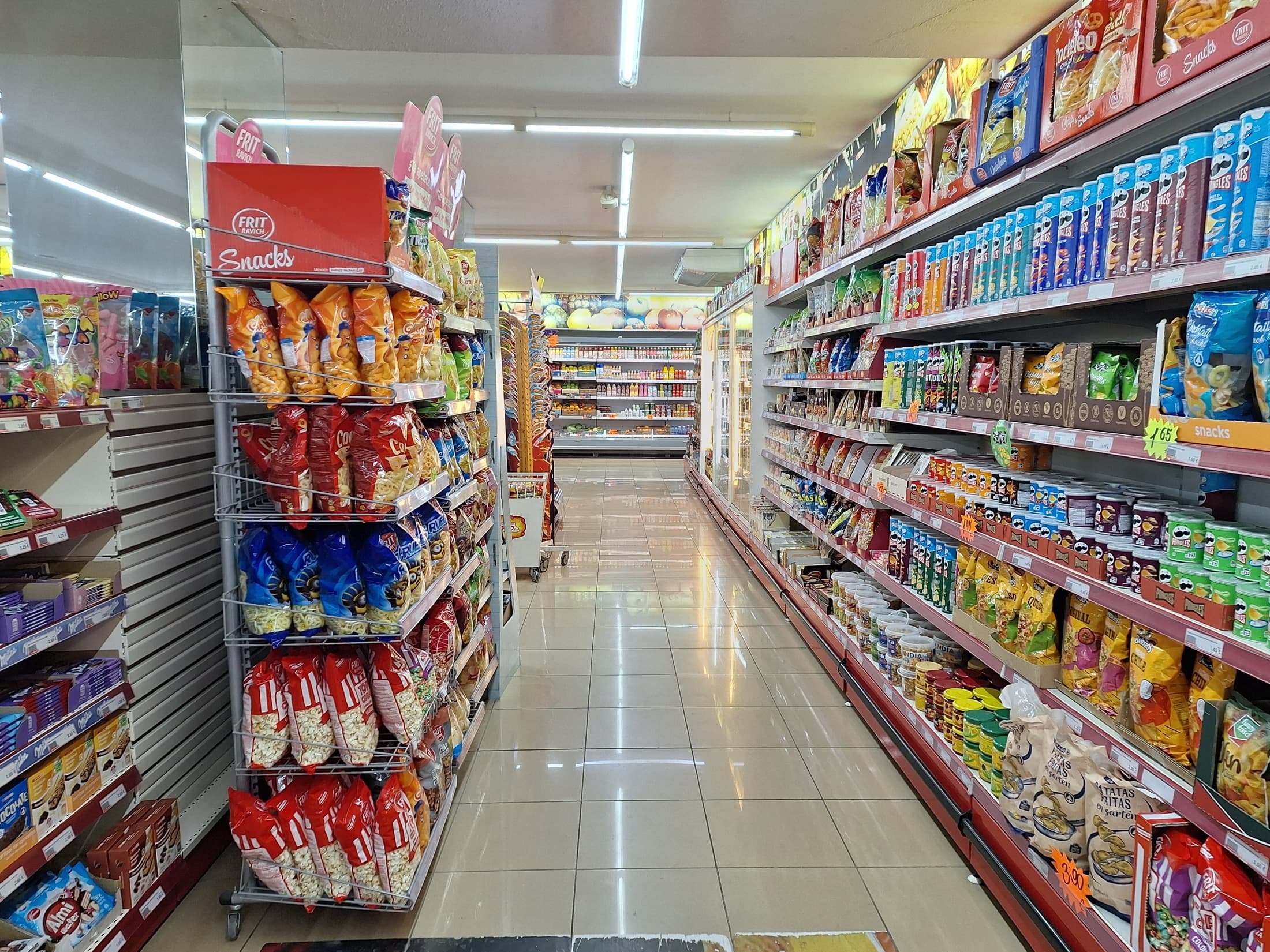 Brightly lit supermarket aisle lined with packaged snacks, chips and boxed products on both sides