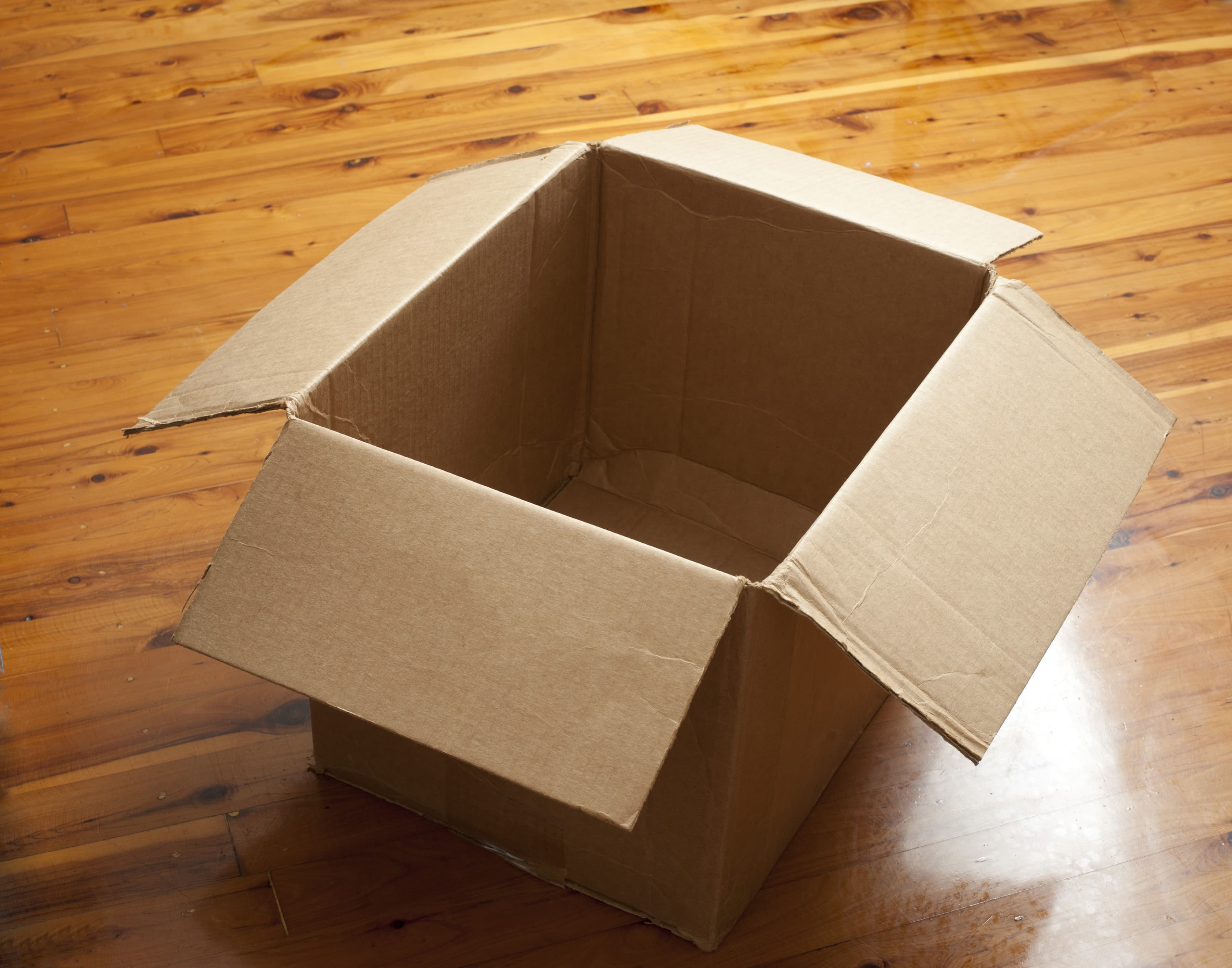 An open empty brown cardboard shipping box on a wooden floor ready to be packed for an ecommerce order