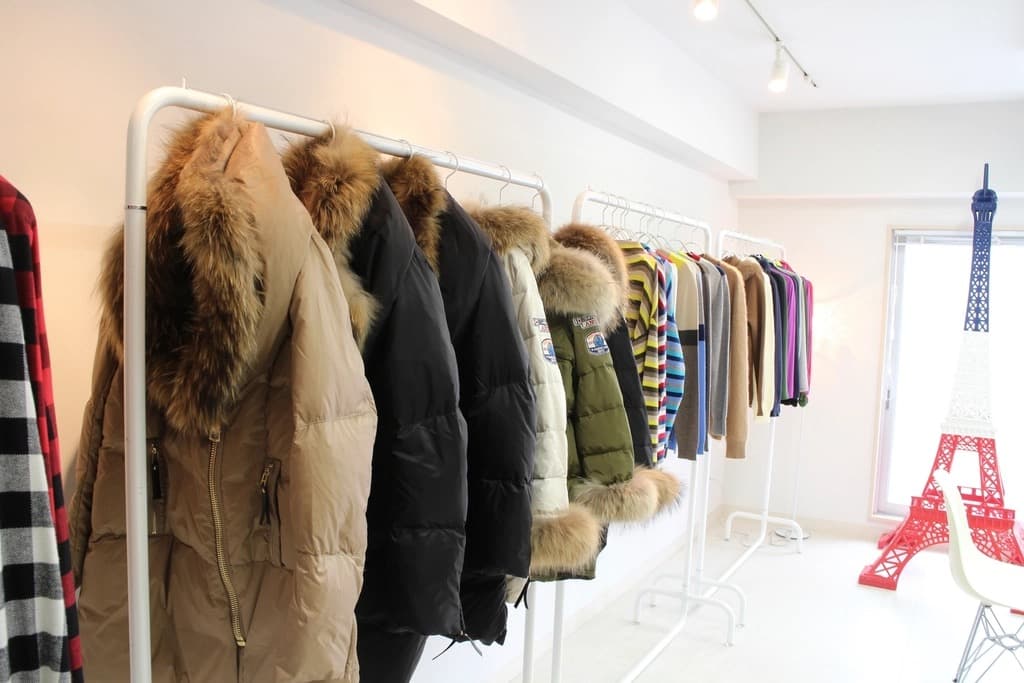Bright apparel store with padded jackets and coats hanging in rows on white clothing racks ready for retail