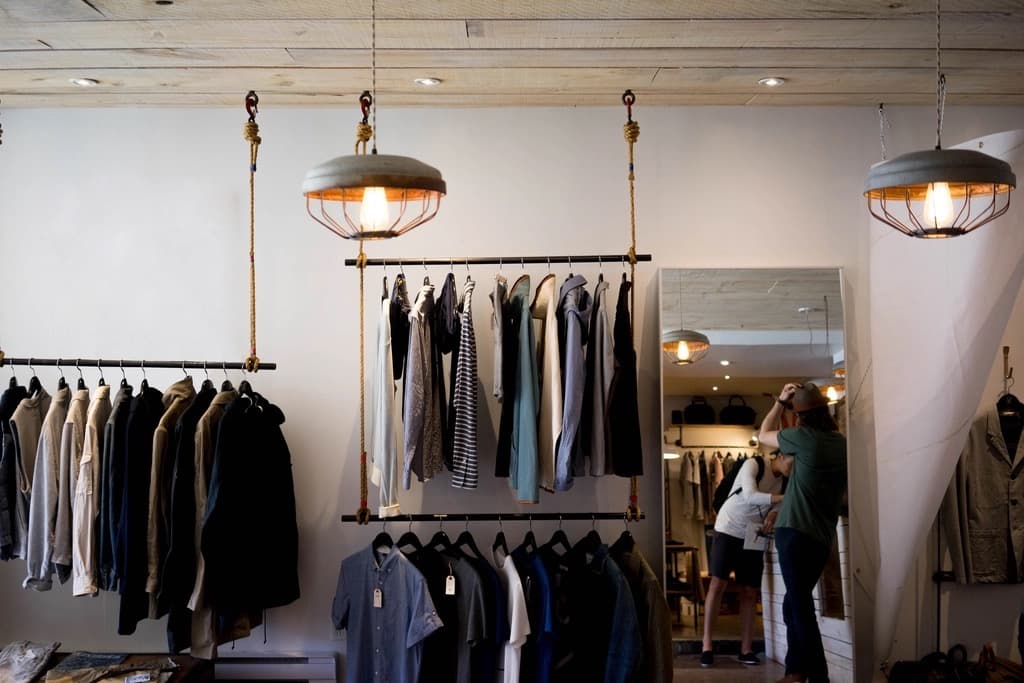 Menswear boutique interior with shirts and jackets neatly hung on wall-mounted rails under industrial pendant lights
