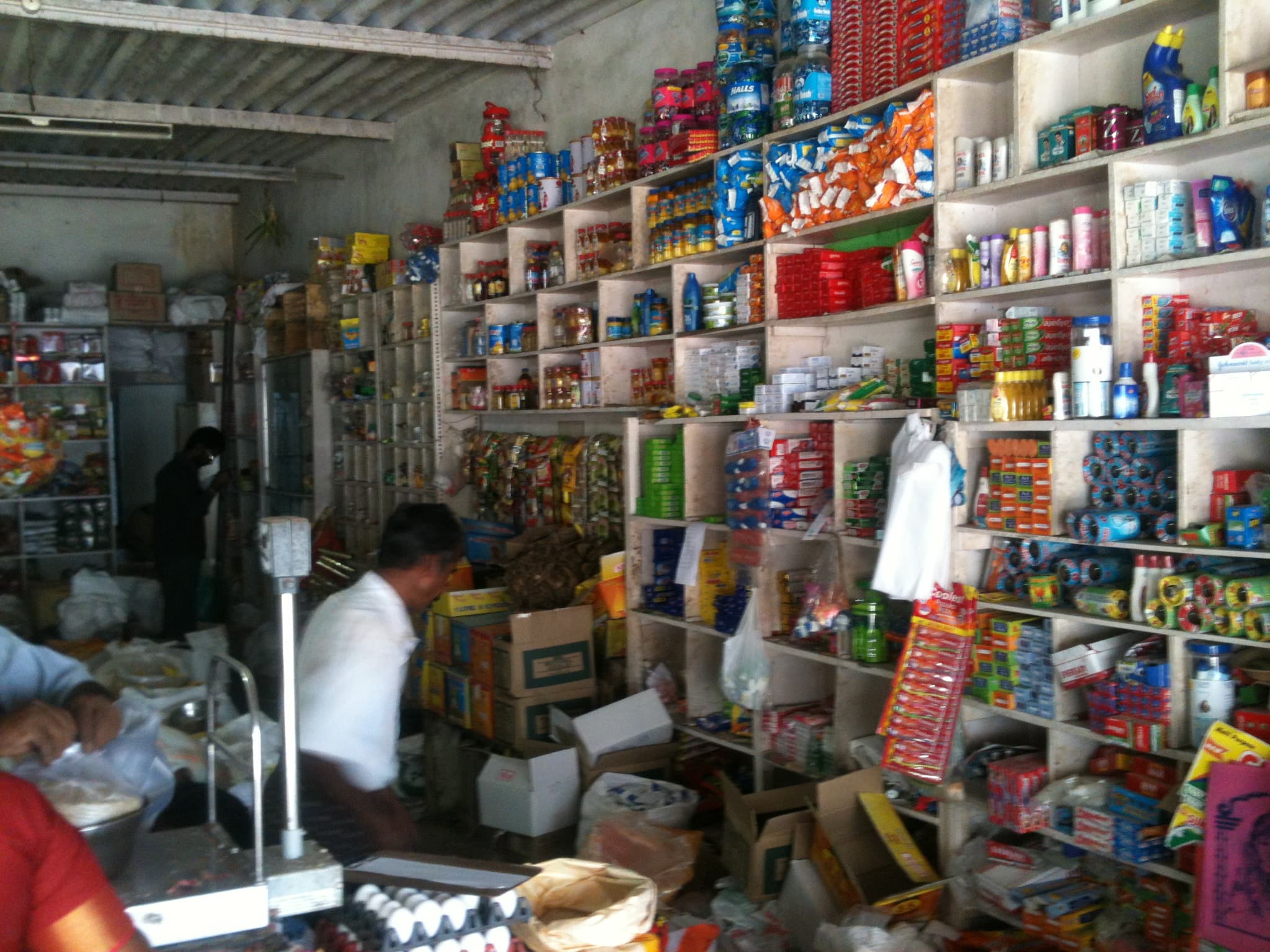 Shopkeeper inside a densely stocked Indian kirana grocery store with floor-to-ceiling shelves of packaged goods