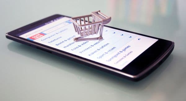 Smartphone showing an online store product category list with a miniature shopping trolley resting on the screen