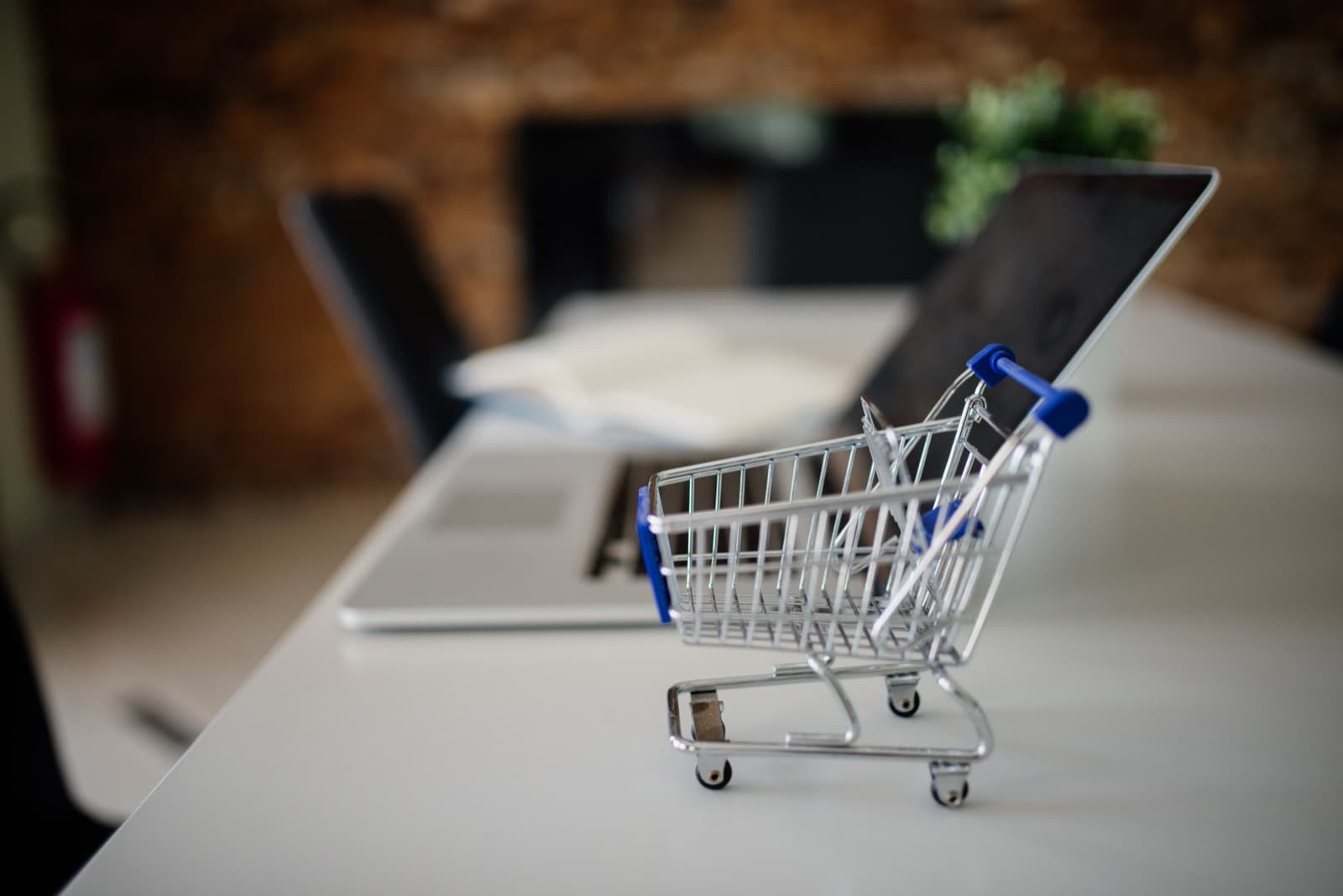 Miniature metal shopping cart on a white desk beside an open laptop