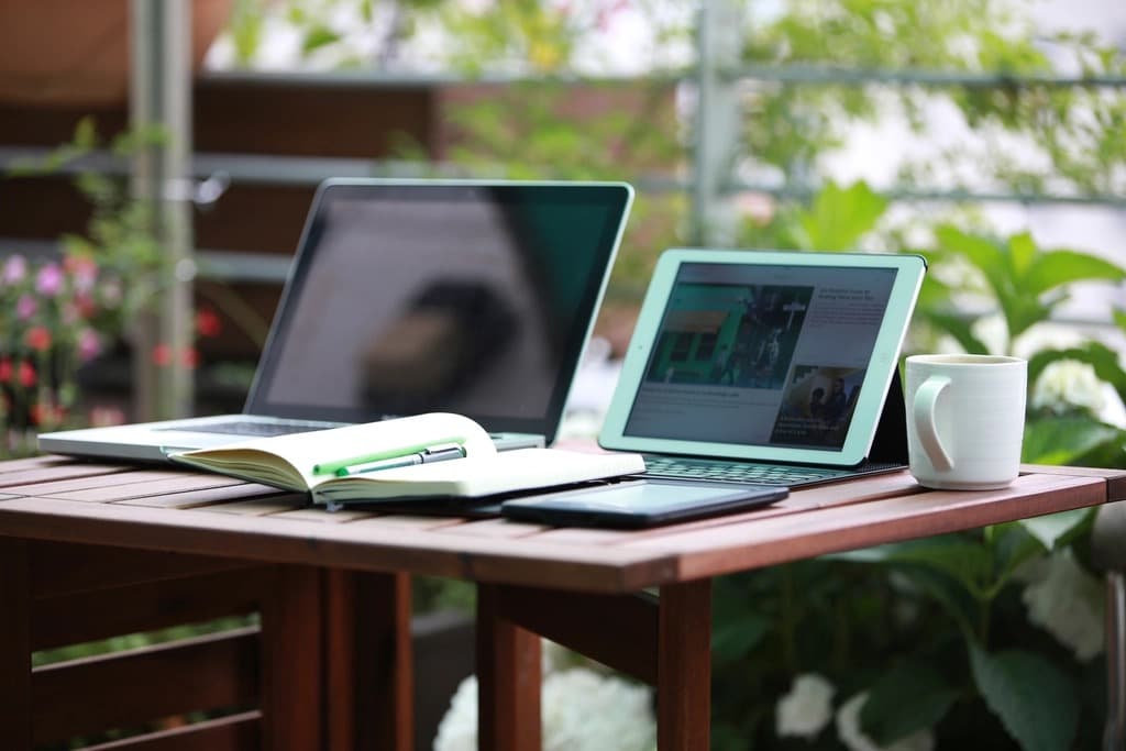 Laptop and tablet on a wooden desk showing an online store website dashboard, with a notebook and coffee cup nearby