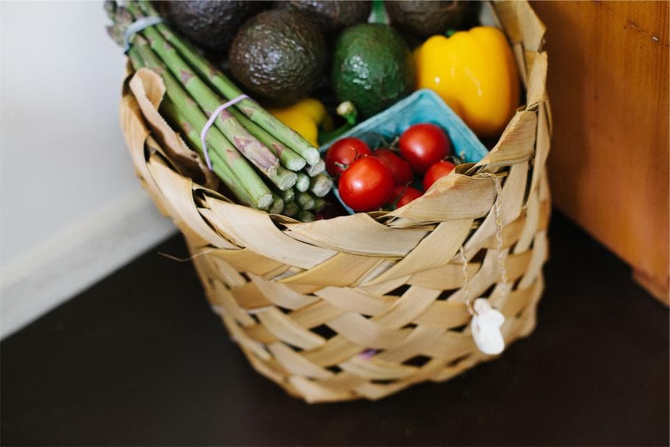 Woven basket filled with fresh asparagus, avocados, cherry tomatoes and a yellow pepper