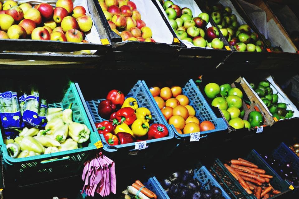 Crates of apples, peppers, oranges, limes and carrots stacked on market shelves