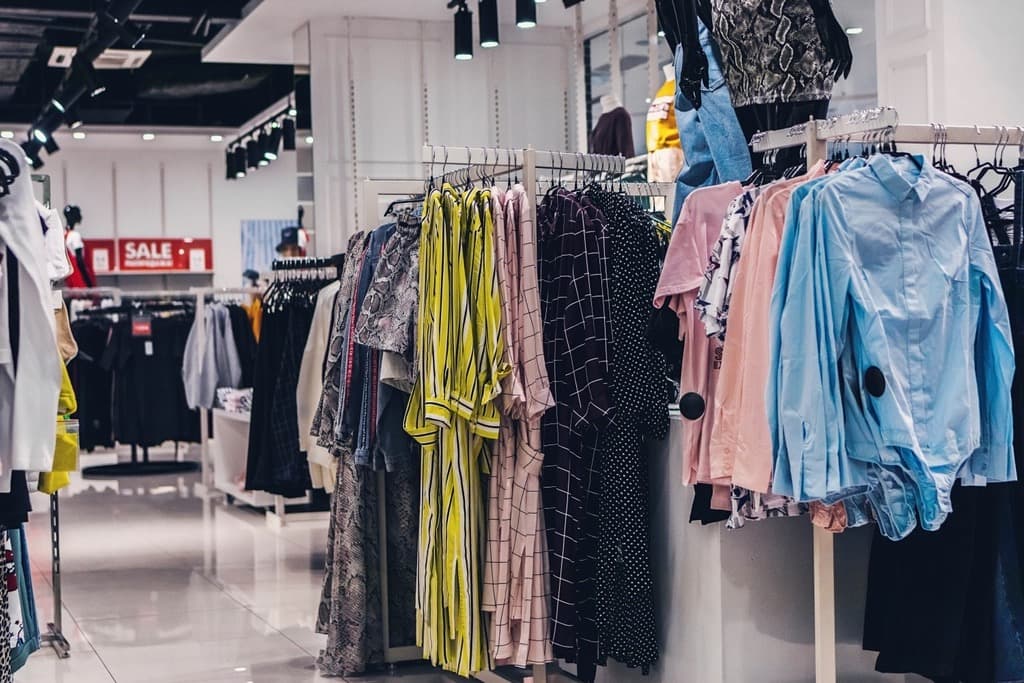Bright fashion store interior with clothing racks of shirts and dresses on hangers