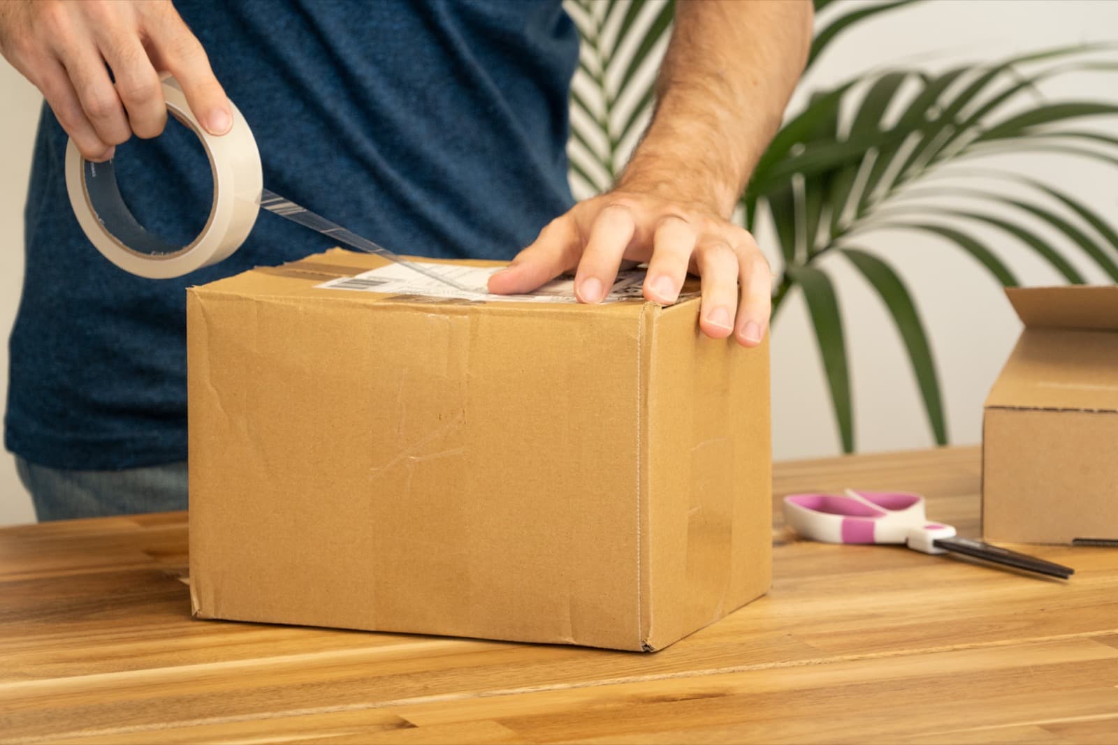 Online seller taping and labelling a cardboard parcel on a desk while preparing a marketplace order for dispatch