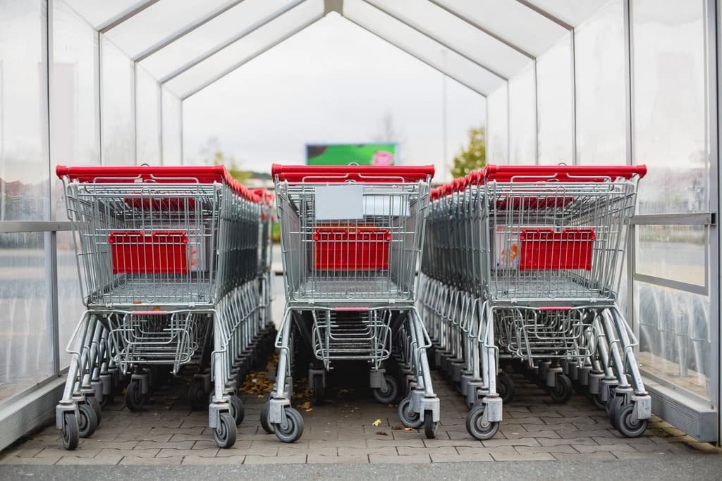 Row of red-handled shopping carts nested outside a bright supermarket entrance
