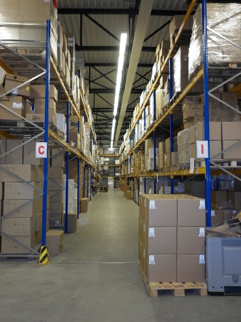 Warehouse aisle with tall racking full of cardboard cartons and pallets of boxes on the floor