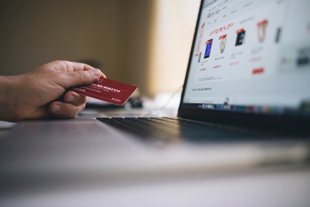 Close-up of a hand holding a payment card in front of a laptop showing an online storefront with discounted products