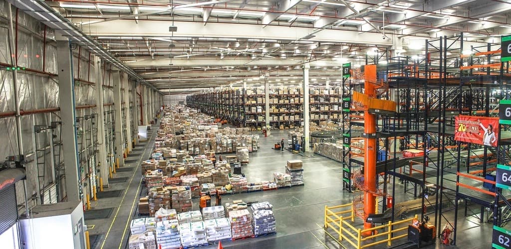 Wide interior view of a large warehouse with long aisles of stacked boxes and tall storage racking