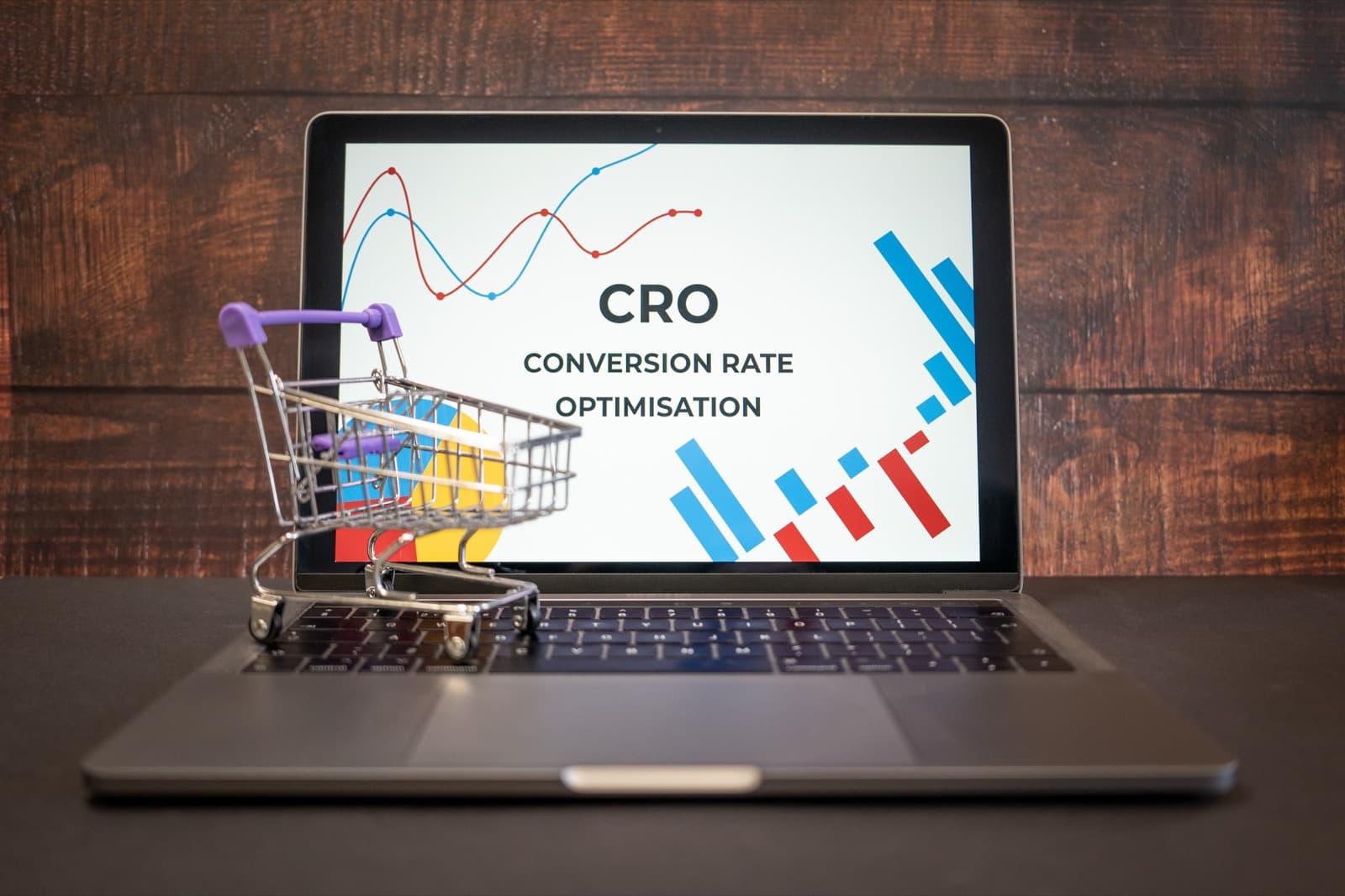 Laptop screen displaying a Conversion Rate Optimisation dashboard with growth charts, next to a miniature shopping cart, for e-commerce website redesign