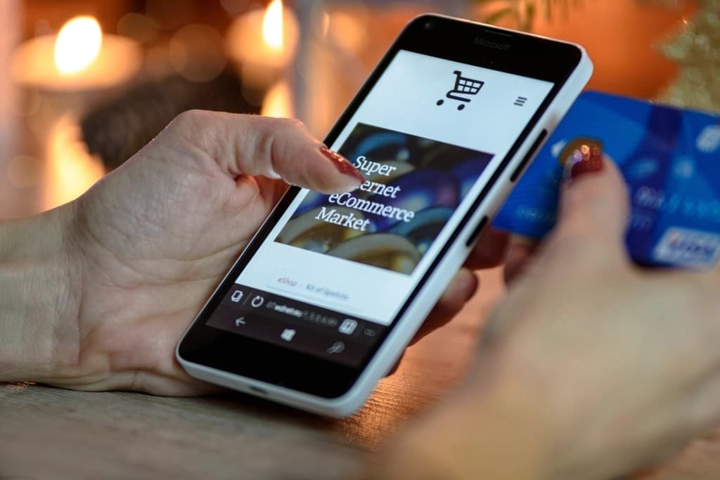 Hand tapping through an eCommerce shopping app on a smartphone while holding a credit card, illustrating one-thumb mobile checkout