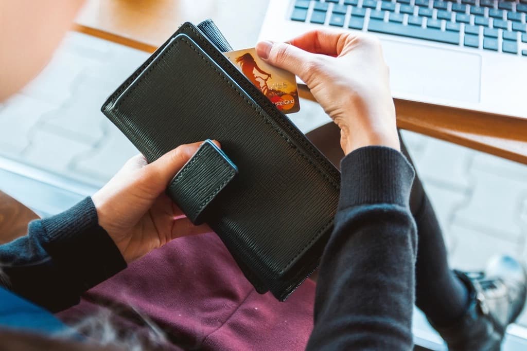 Person taking a credit card from a wallet in front of an open laptop to pay for an online purchase, illustrating secure e-commerce website checkout