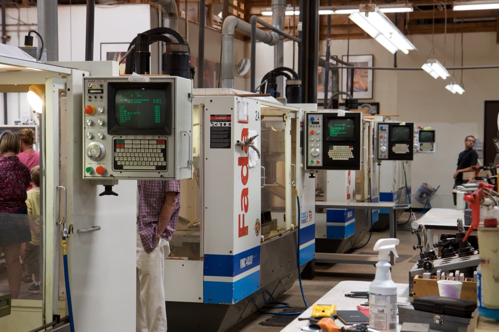 Row of CNC vertical milling machines with control panels lit up on a factory floor, a worker leaning into the nearest machine