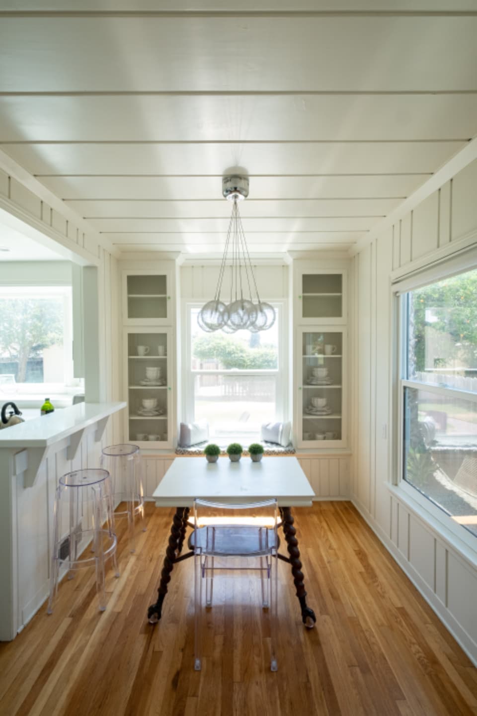 Sunlit white breakfast nook and kitchen with wood floor and window seat, a property interior featured in a listing app gallery