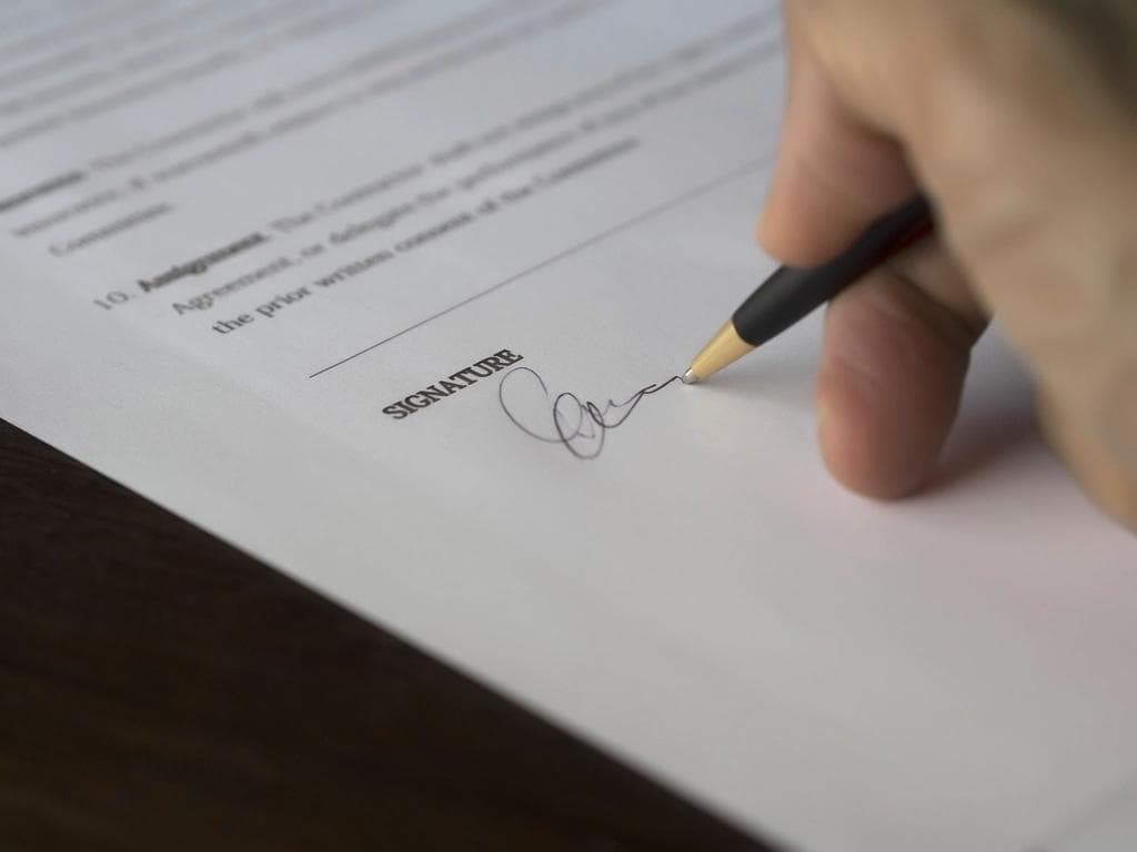 Hand signing a property agreement contract on the signature line with a pen, representing in-app e-signature of a lease or transaction