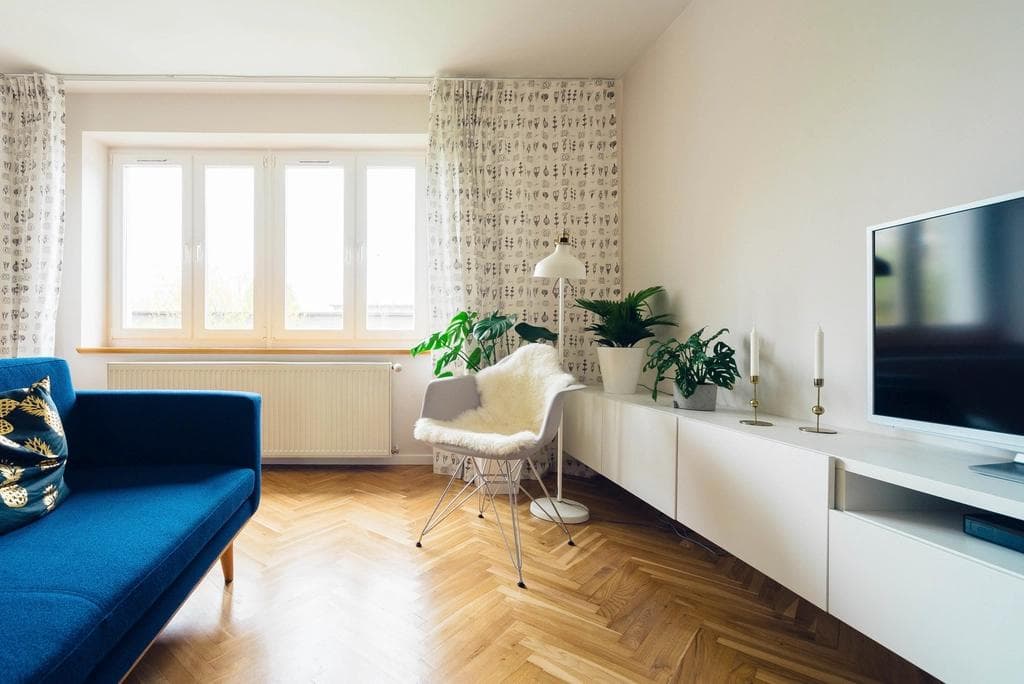 Bright modern living room with a blue sofa, herringbone wood floor and large window, the kind of property interior shown in a listing or 3D virtual tour